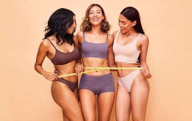 How to Boost Your Confidence With Figure Enhancing Pieces 3 Group of diverse women in lingerie laughing and measuring waist with tape.