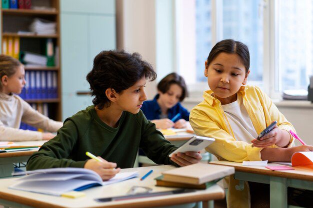 Two students in a classroom comparing answers on calculators while working on notebooks at their desks.