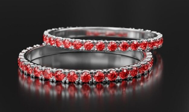 Two silver rings with red gemstones, stacked and shining on a dark reflective background.
