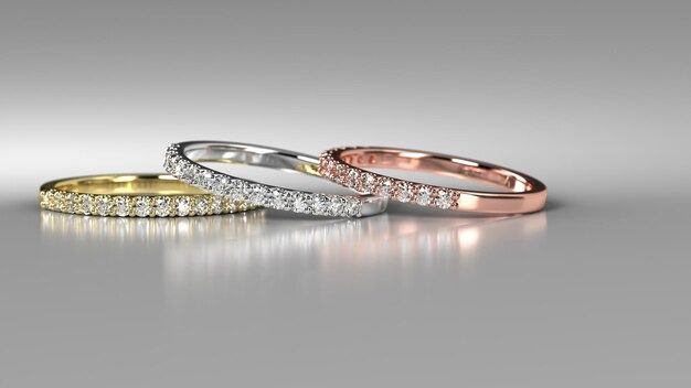Three slim diamond bands in yellow, white, and rose gold arranged side by side on a neutral surface.